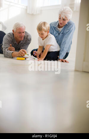 Young boy sitting on the floor with his grandparents and drawing with crayons. Stock Photo
