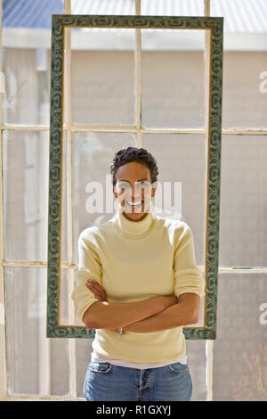 Portrait of a laughing mid-adult woman standing in front of a window with her arms crossed. Stock Photo