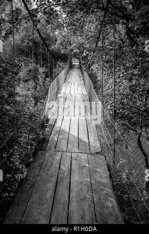 Old suspension footbridge covered with wooden planks in the village of Debnevo, Stara Planina mountain, Bulgaria. Black and white picture, nice perspe Stock Photo