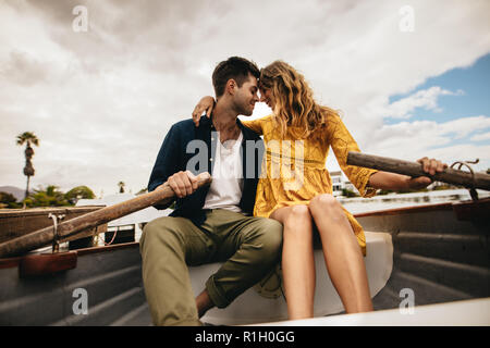 Couple in love sitting in a boat relaxed holding each other. Young couple sitting together in a boat touching their heads holding the paddles. Stock Photo