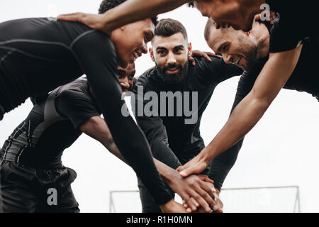 Low angle view of footballers talking about the game plan standing in a huddle. Soccer players holding their hands standing in a huddle and cheering t Stock Photo