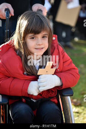 Young girl with poppy cross in wheelchair attending Remembrance Sunday, War Memorial, Bordon, Hampshire, UK. 11.11.2018.