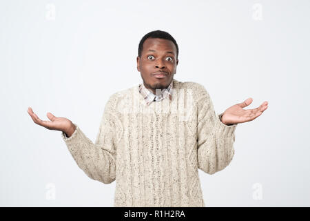 doubtful african man in sweater shrugs shoulders with confusion Stock Photo