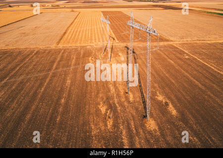 High voltage electricity pylons for power transmission in field from drone pov Stock Photo