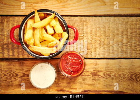 top view of delicious french fries in a red pot with sauces on an old wooden table Stock Photo