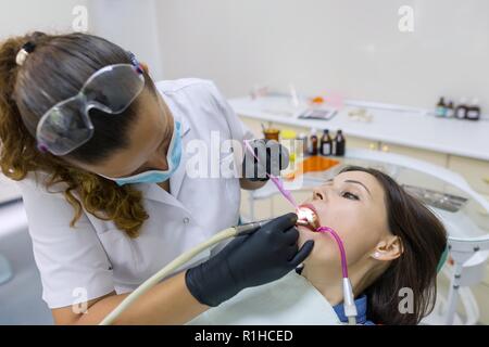 Medicine, dentistry and healthcare concept. Female dentist using dental curing UV lamp on teeth of patient. Stock Photo