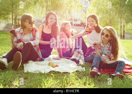 Rest in the park. Mothers with children sit on the grass, women drink coffee, children eat apples Stock Photo