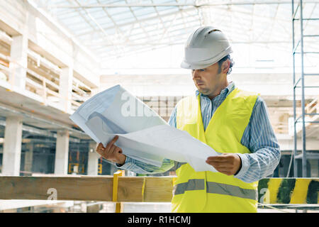 Portrait of male engineer at construction site. Builder looks at the plan of the construction site. Building, development, teamwork and people concept Stock Photo