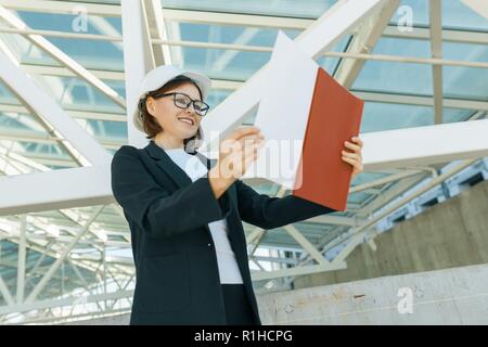 Portrait of mature architect woman at construction site reading blueprint. Building, development, teamwork and people concept. Stock Photo