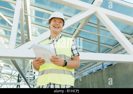 Portrait of male engineer at construction site. Builder looks at the plan of the construction site. Building, development, teamwork and people concept Stock Photo