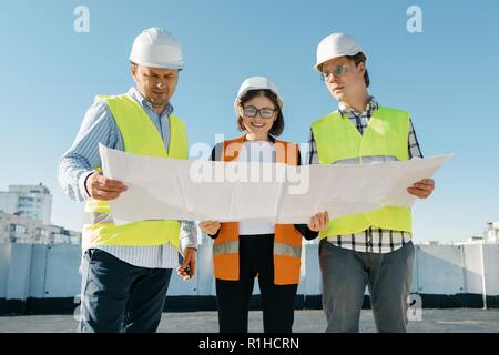 Team of builders engineers at a construction site, reading blueprint. Construction, development, teamwork and people concept. Stock Photo