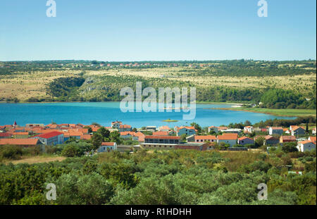 Crkva Sveti Duh church in Posedarje in Novigradsko More bay in blue azure water against the background of a hill, green trees and houses with red roof Stock Photo