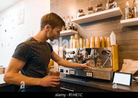 Young male barista makes a drink near the coffee machine. Coffee shop business concept. Stock Photo