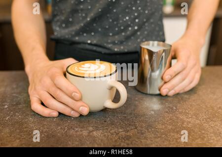 Closeup of latte art, hands of barista and iron mug with milk, background coffee house. Stock Photo