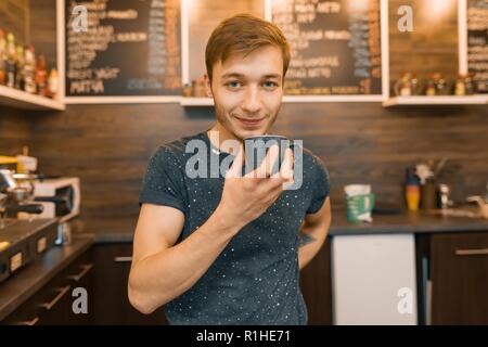 Young smiling male barista drinks coffee in coffee shop, man enjoys fresh fragrant coffee. Stock Photo