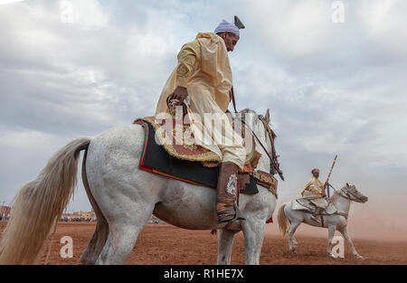 a group of horse riders, wearing traditional clothes and charging along a straight path in a show called Tbouria or Fantasia Stock Photo