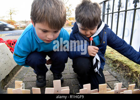 Youngsters perusing the crosses & poppies laid on Remembrance Sunday, War Memorial, Bordon, Hampshire, UK. 11.11.2018.