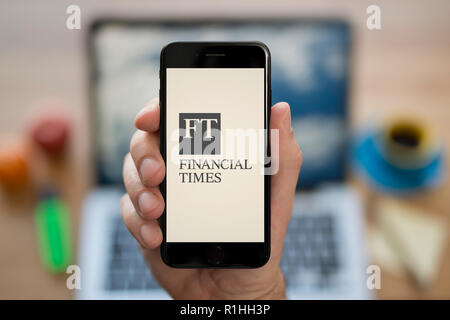 A man looks at his iPhone which displays the Financial Times logo, while sat at his computer desk (Editorial use only). Stock Photo