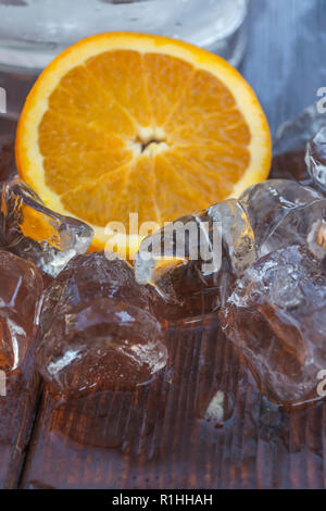 Detailed ,close up view of ice cubes on wood table, to defrost, slice of orange on background... Stock Photo