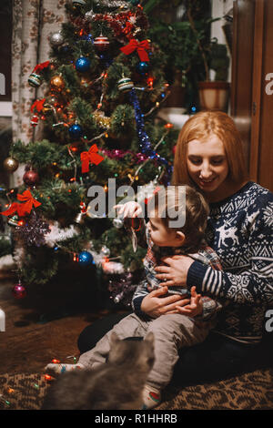 Happy mother and son sitting beside Christmas tree at home during Christmas holidays Stock Photo