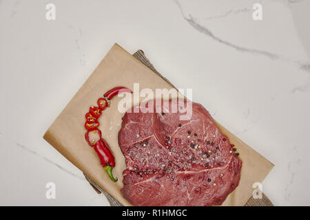 top view of fresh raw meat on baking paper with chopped chilli pepper on white background Stock Photo