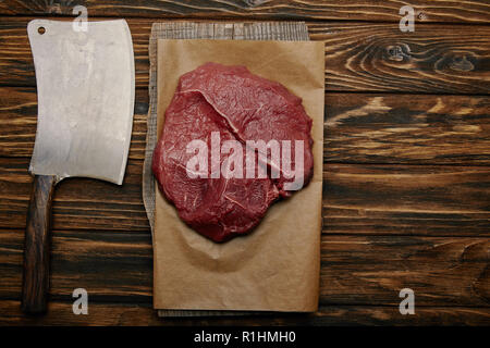 top view of raw meat on baking paper with butcher knife on wooden background Stock Photo