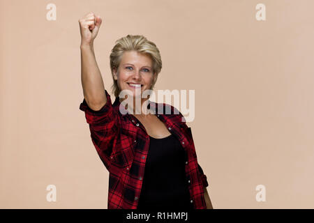 Smiling blonde woman giving victory gesture wearing checked red shirt Stock Photo