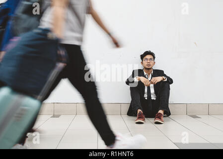 dowdy young asian businessman sitting at walkway thinking of his problem and look so depressed while people passing by ( motion blur ) Stock Photo