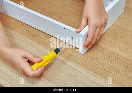 The furniture assembler tightens the screw into a wooden chipboard drawer using a screwdriver, ready-to-assemble furniture. Stock Photo
