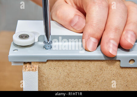 The assembly worker tightens the screw into the drawer slide brackets of the  drawer made of the chipboard with a screwdriver, ready-to-assemble furni Stock Photo