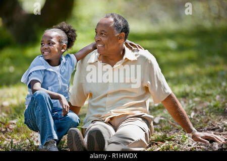 Happy young girl sitting with her grandfather in a park. Stock Photo