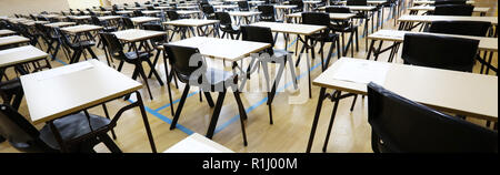 View of large exam room hall and examination desks tables lined up in rows ready for students at a high school to come and sit their exams tests paper Stock Photo