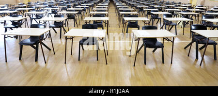 View of large exam room hall and examination desks tables lined up in rows ready for students at a high school to come and sit their exams tests paper Stock Photo