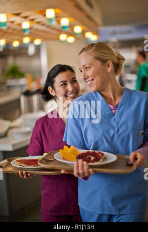 Two young nurses smile and chat together as they get their lunch from the hospital canteen. Stock Photo