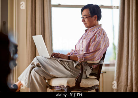 Happy middle aged man working on a laptop computer in his home office. Stock Photo
