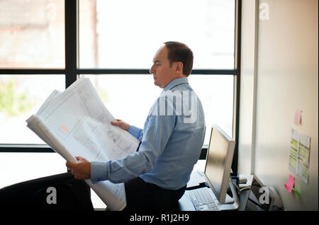 Businessman leans on desk looking at building plans. Stock Photo