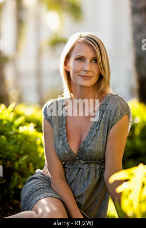 Mid adult woman sitting under palm trees during her summer vacation. Stock Photo