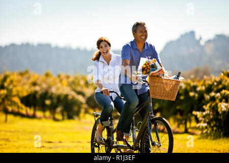 Middle-aged woman having fun riding the bicycle with her husband in the vineyard. Stock Photo