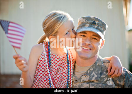 Portrait of a smiling soldier being kissed on the cheek by his young daughter. Stock Photo