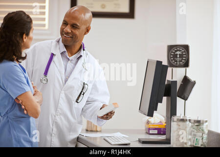 Smiling male doctor having a conversation with a female nurse over a box of medication inside his office. Stock Photo