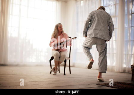 Senior man dancing while his wife plays a guitar. Stock Photo
