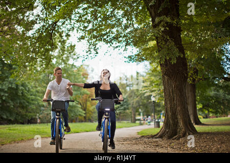 Smiling young couple riding bikes through a city park. Stock Photo
