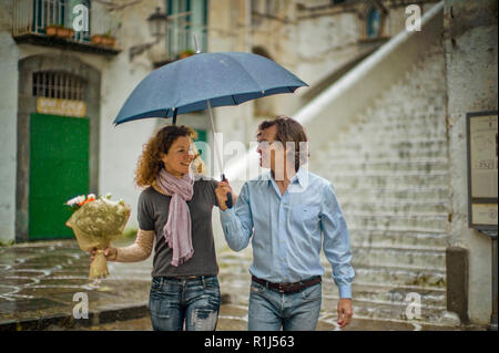 Smiling middle aged couple sheltering under an umbrella. Stock Photo