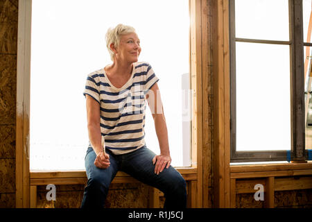Smiling mature woman sits in a house under construction. Stock Photo