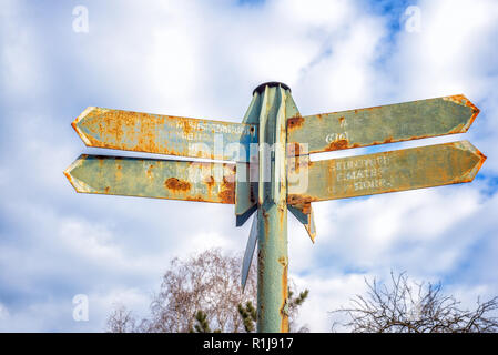 Old rusty street sign with arrows with clouds in background Stock Photo