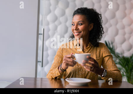 Beaming dark-eyed woman looking at window while drinking some coffee Stock Photo