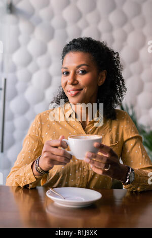 Stylish woman wearing accessories and yellow blouse drinking coffee Stock Photo