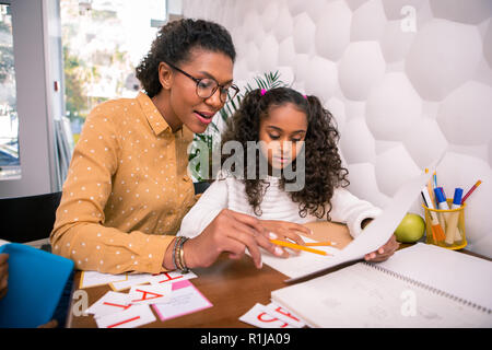 Smart caring teacher teaching cute preschool girl reading and writing Stock Photo