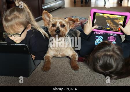 Sisters playing on their tablets while cuddling with their best friend Stock Photo