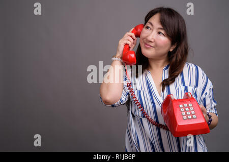 Mature beautiful Asian businesswoman holding old red phone Stock Photo